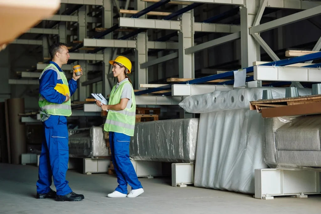 Two people wearing high-visibility vests talking inside an industrial building