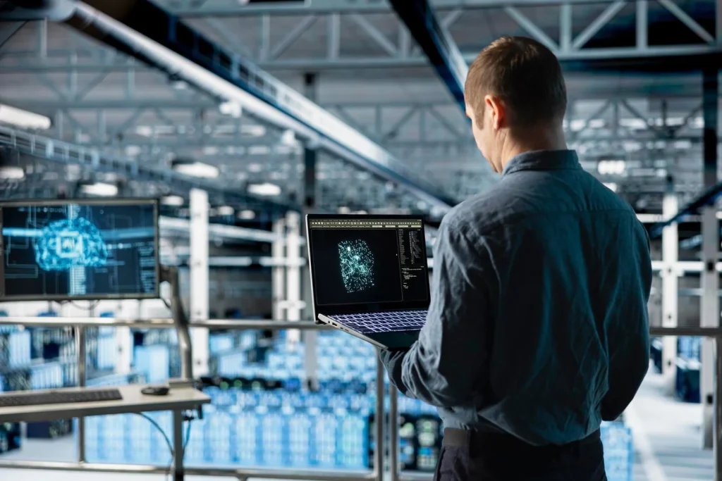 Technical worker using a laptop to review digital system visualizations in an industrial setting