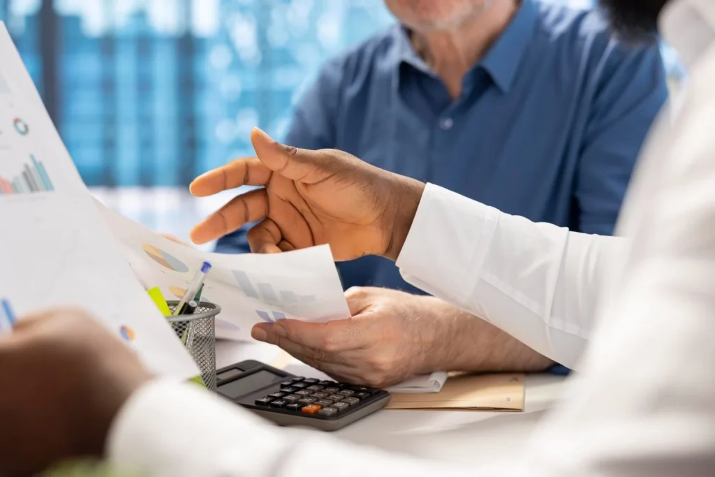 A team reviews charts and paperwork beside a calculator during a cost discussion.