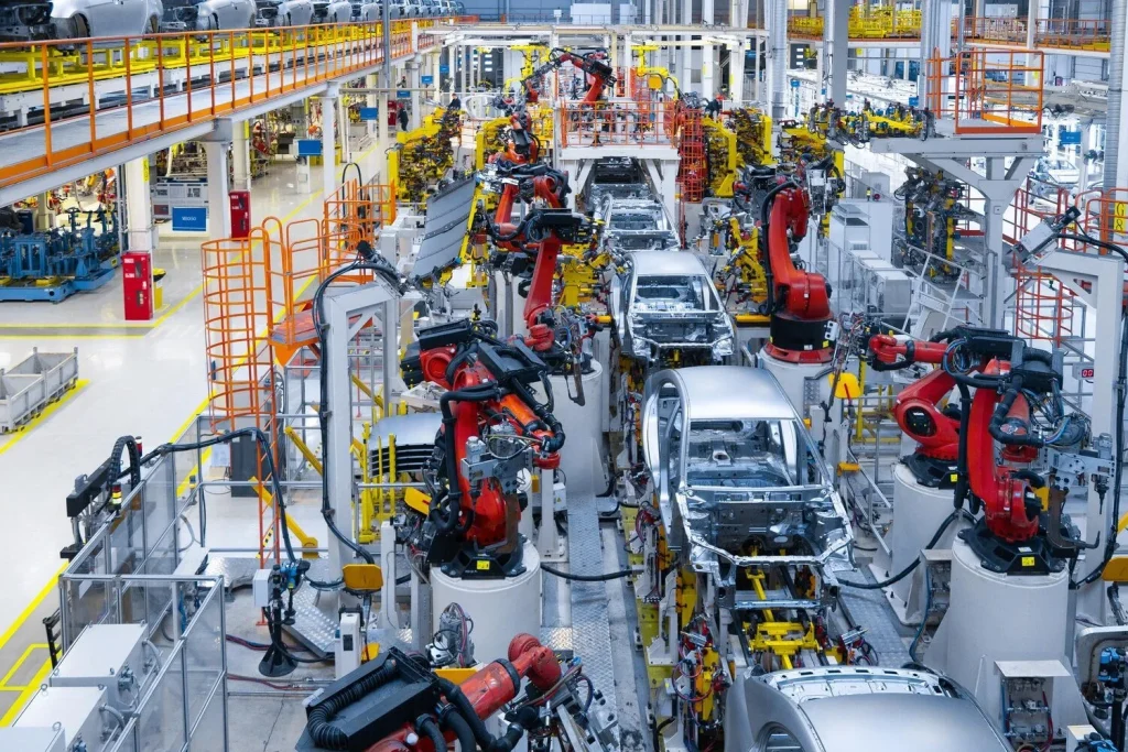 Robotic arms positioned around vehicle bodies on an automotive assembly line.