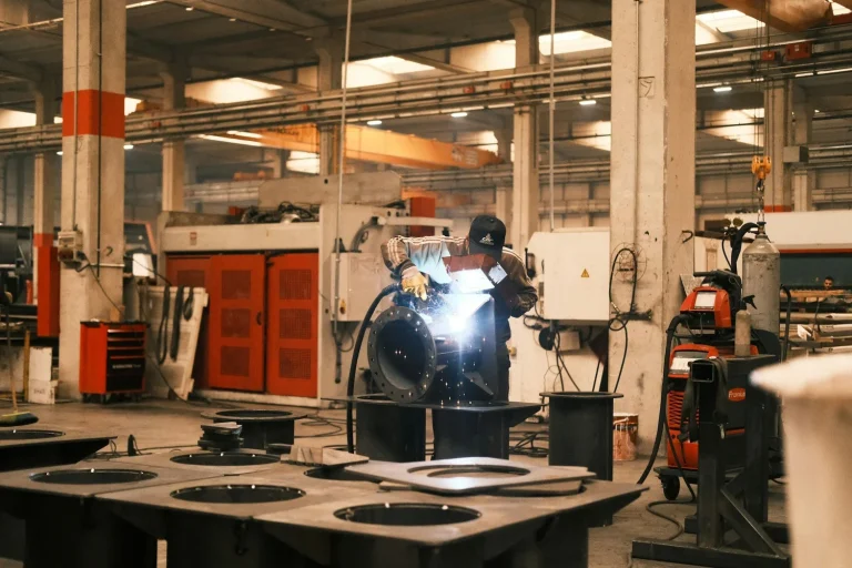 Worker welding a metal component inside an industrial production facility.